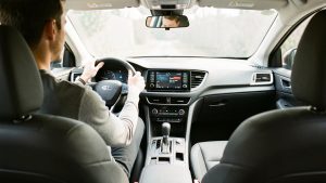 Habitacle automobile moderne vu depuis le siège conducteur : un homme est installé confortablement, avec des équipements ergonomiques visibles et une ambiance sobre sous une lumière naturelle.