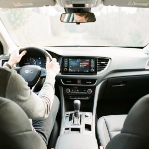 Habitacle automobile moderne vu depuis le siège conducteur : un homme est installé confortablement, avec des équipements ergonomiques visibles et une ambiance sobre sous une lumière naturelle.