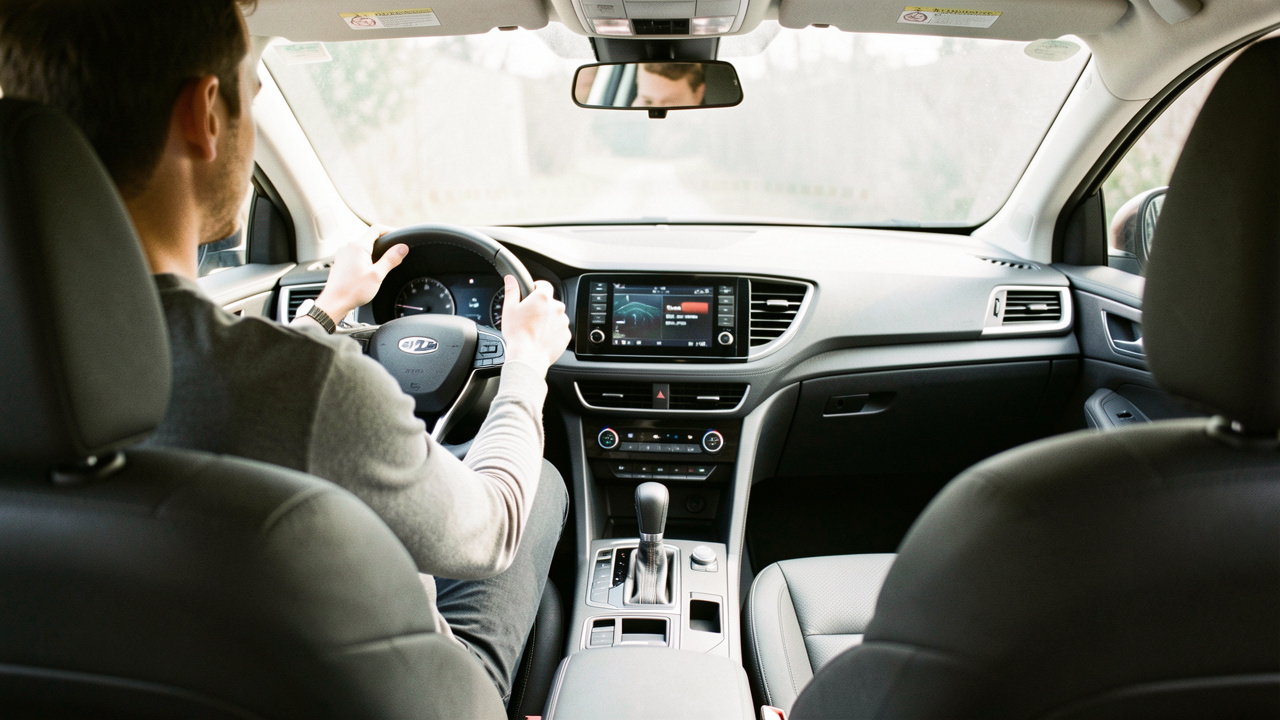 Habitacle automobile moderne vu depuis le siège conducteur : un homme est installé confortablement, avec des équipements ergonomiques visibles et une ambiance sobre sous une lumière naturelle.