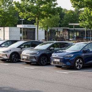 SUV hybrides compacts et familiaux stationnés en rangée sur une aire d’autoroute française, éclairés par une lumière naturelle.
