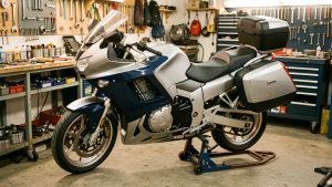 Moto de tourisme routière argentée et bleu foncé inspectée dans un atelier mécanique propre et organisé.
