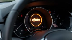 Gros plan réaliste sur le tableau de bord d’une voiture compacte, avec un voyant orange rond représentant une silhouette de véhicule.