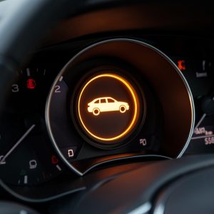 Gros plan réaliste sur le tableau de bord d’une voiture compacte, avec un voyant orange rond représentant une silhouette de véhicule.